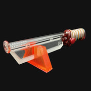 710 Pipes Smoke Shop MD Glass x Kadabra collaboration glass pipe with red accents and striped handle on an orange resin stand.