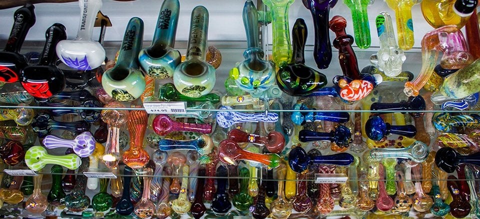 Shelf display of many colorful glass pipes in a row