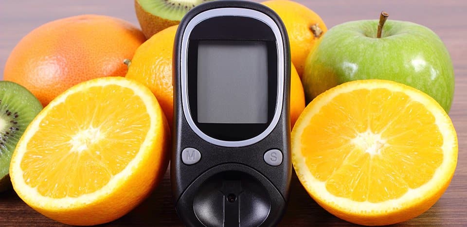 Blood glucose meter surrounded by oranges and an apple