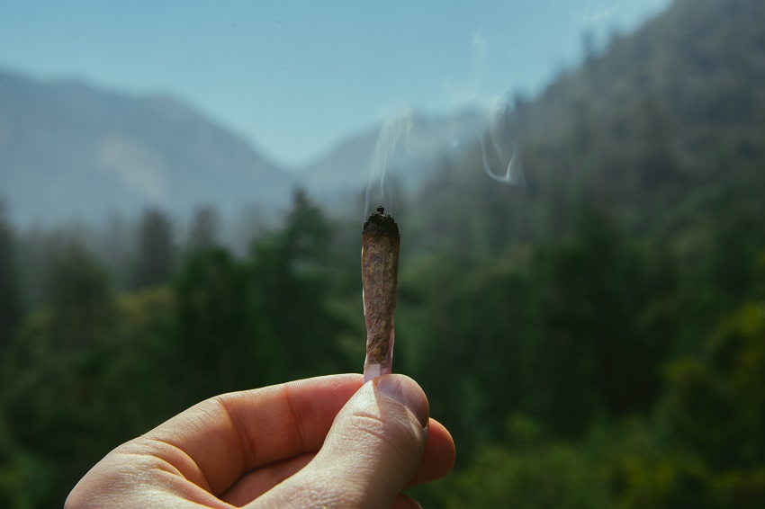 Hand Holding Lit Joint with Billowing Smoke in Front of Scenic Rocky Mountain View