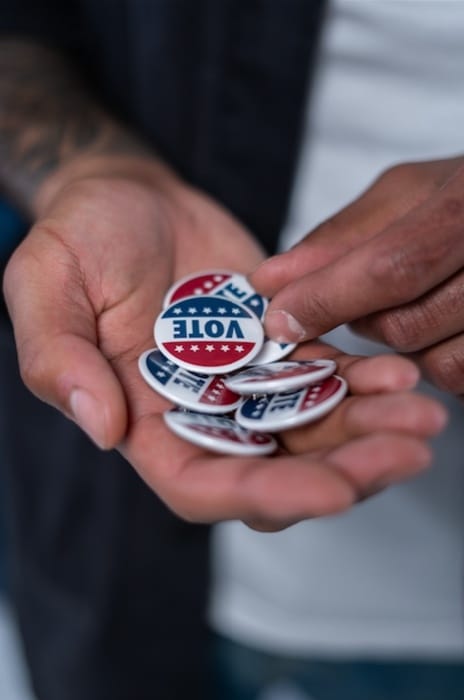 Hand holding 'VOTE' pins to give to millennial voters at polling center