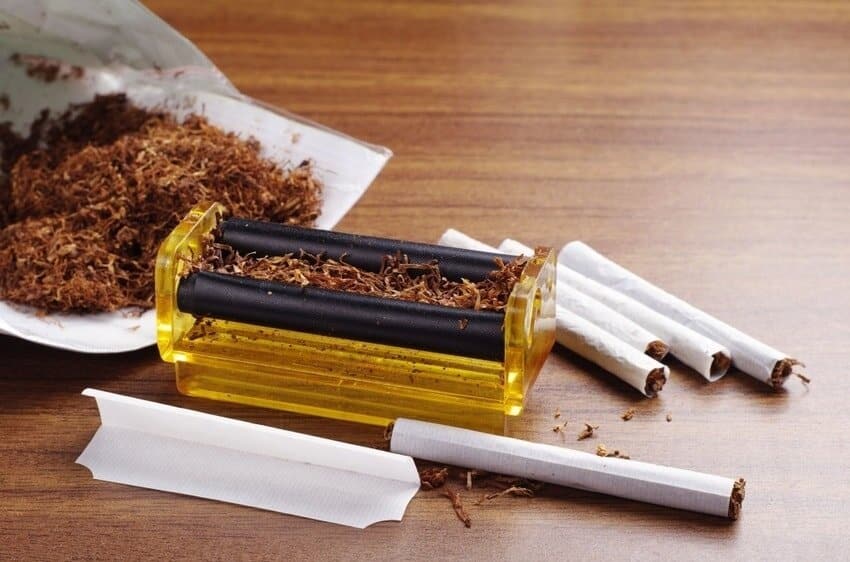 Rolling papers, loose tobacco and a rolling machine on a wood table