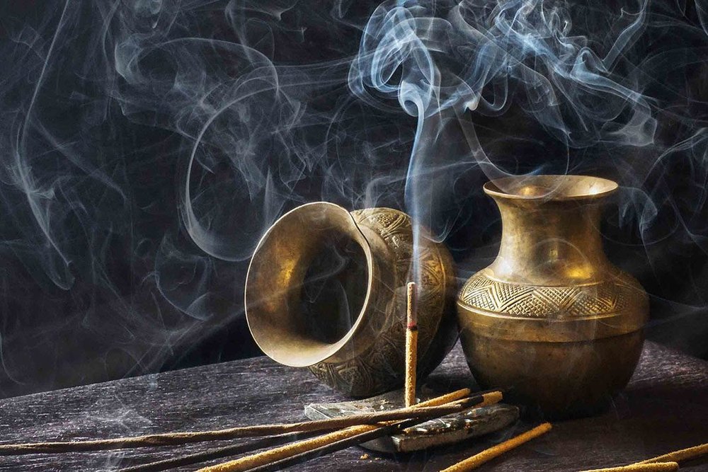 Stick of burning incense, brass vases and billowing smoke