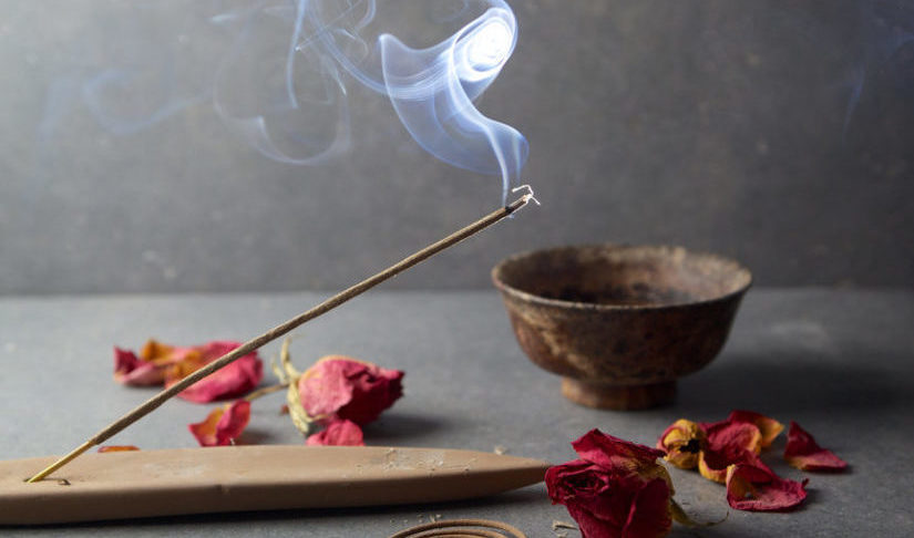 Incense stick burning on wooden holder beside dried roses