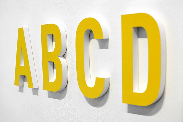 Large yellow alphabet letters hung on white gallery wall