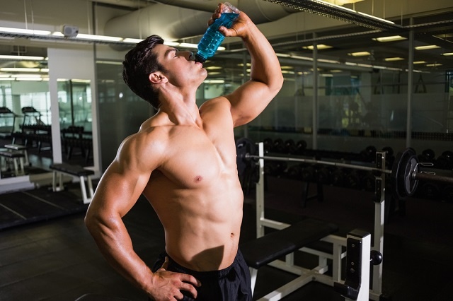 Muscular shirtless man chugging energy drink in gym