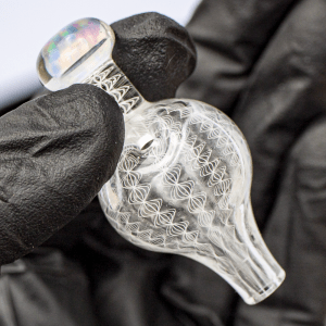Black gloved hand holding Mycomann engraved glass bubble cap with opal handle.