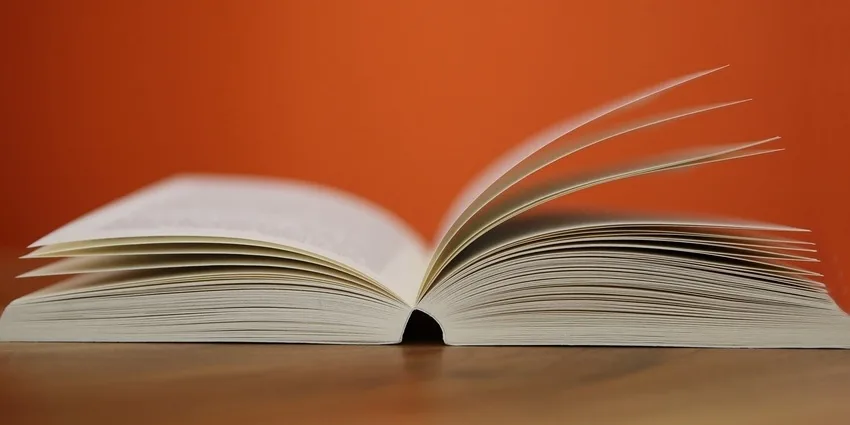 Book of terminology open on table beside bright orange wall