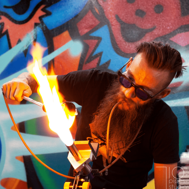 Glass artist working with a torch flame against a colorful graffiti background