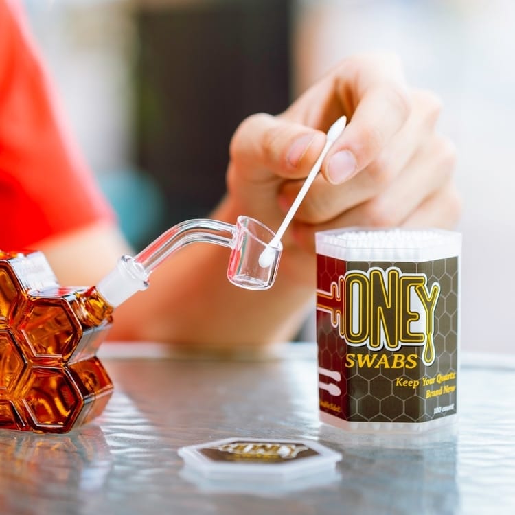 Person using stainless steel dab tool to move wax concentrate from storage container to heady glass dab rig