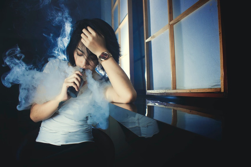 Woman holding e-cigarette while vaping indoors