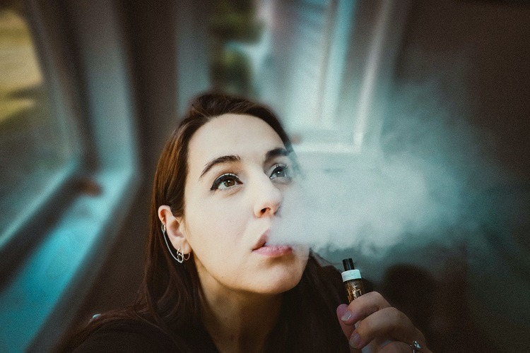 Woman holding vaporizer exhales vape cloud