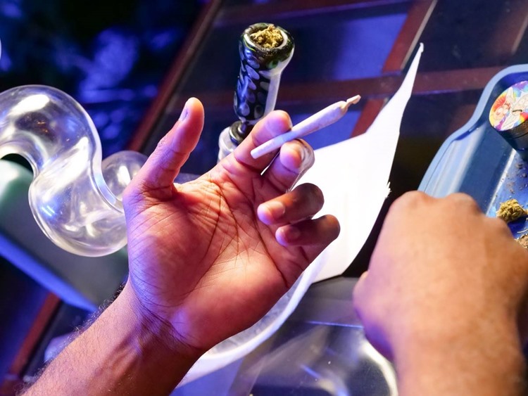 Hand holding rolled joint beside heady glass bong and rolling tray with metallic grinder