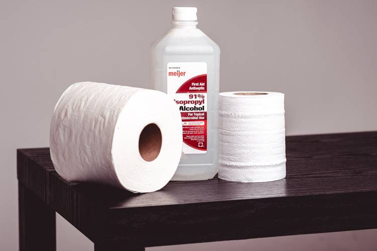 Isopropyl alcohol bottle and toilet paper rolls on wooden table.