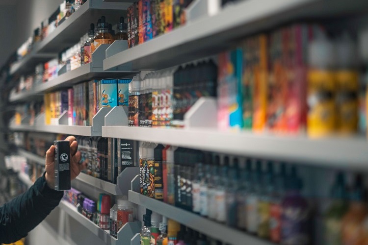 Customer holding black ejuice box beside shelves of vaporizers and accessories in vape shop