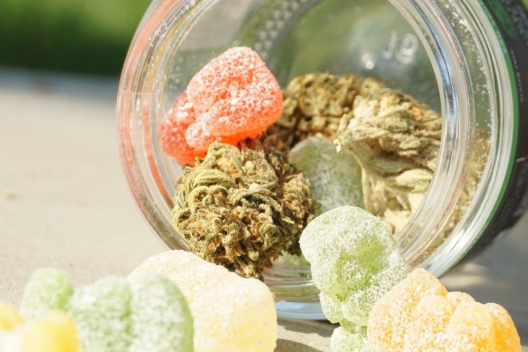 Overturned mason jar containing cannabis nuggets and multicolored edible gummies
