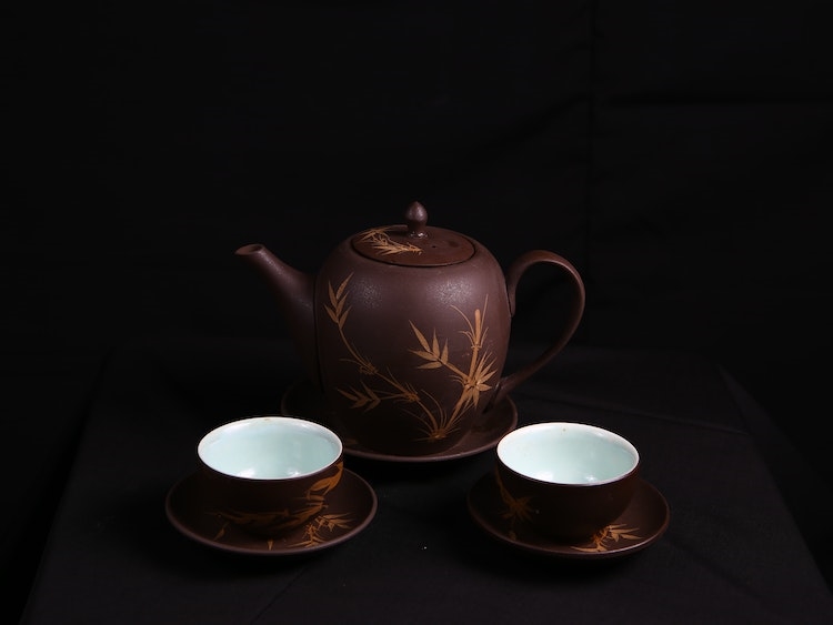 Brown teapot with engraved floral designs and two adjacent teacups