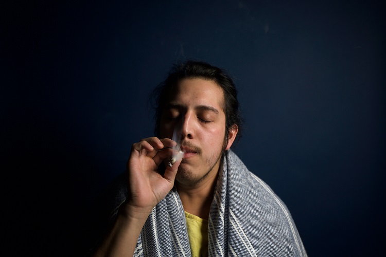 Man smoking rolled cannabis joint with blanket on shoulders
