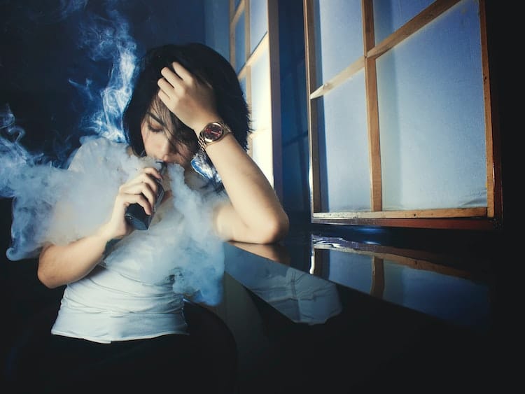 Woman using vape mod in dark room beside window