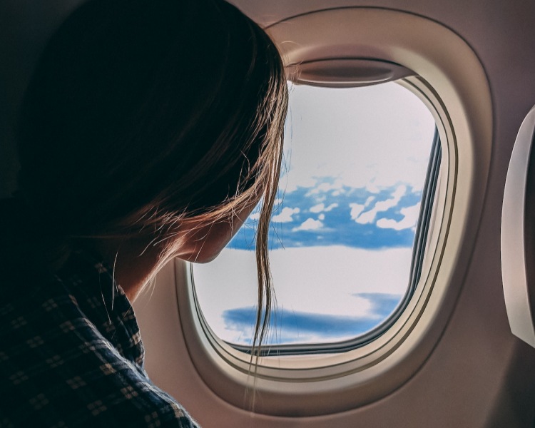 Woman in airplane window seat looking out window at cloudy blue sky