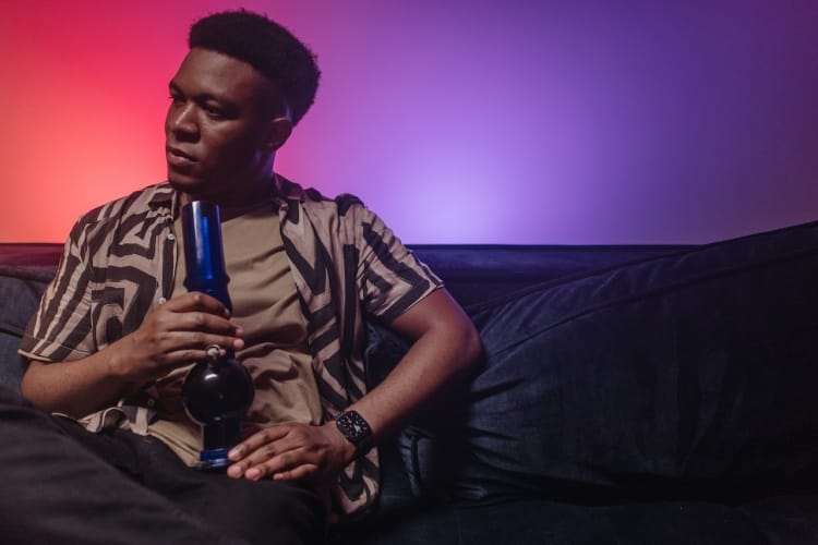 Man smoking bong on sofa in room with purple and red colored lighting