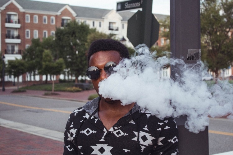 Man exhaling vaporizer cloud outdoors beside stop sign at intersection