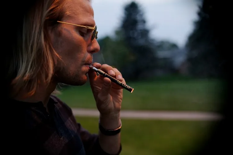 Blond man in aviator sunglasses using vaporizer pen outdoors
