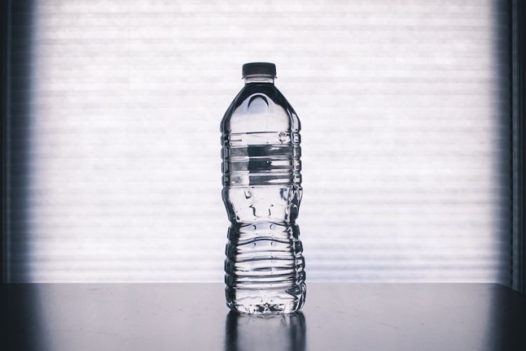 Clear plastic water bottle on black tabletop with closed blinds on window in background