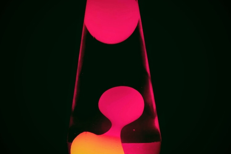 Lava lamp with glow-in-the-dark pink and orange interior segments lit by blacklight in a dark room
