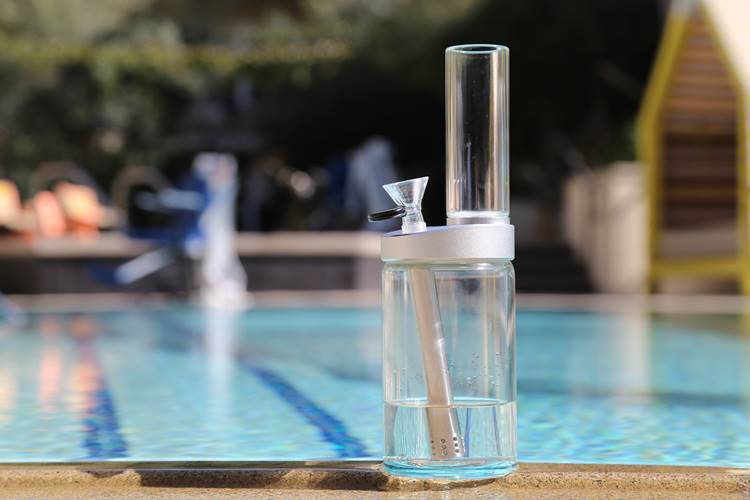Large, transparent bong on the concrete ledge of the outdoor pool on a sunny day