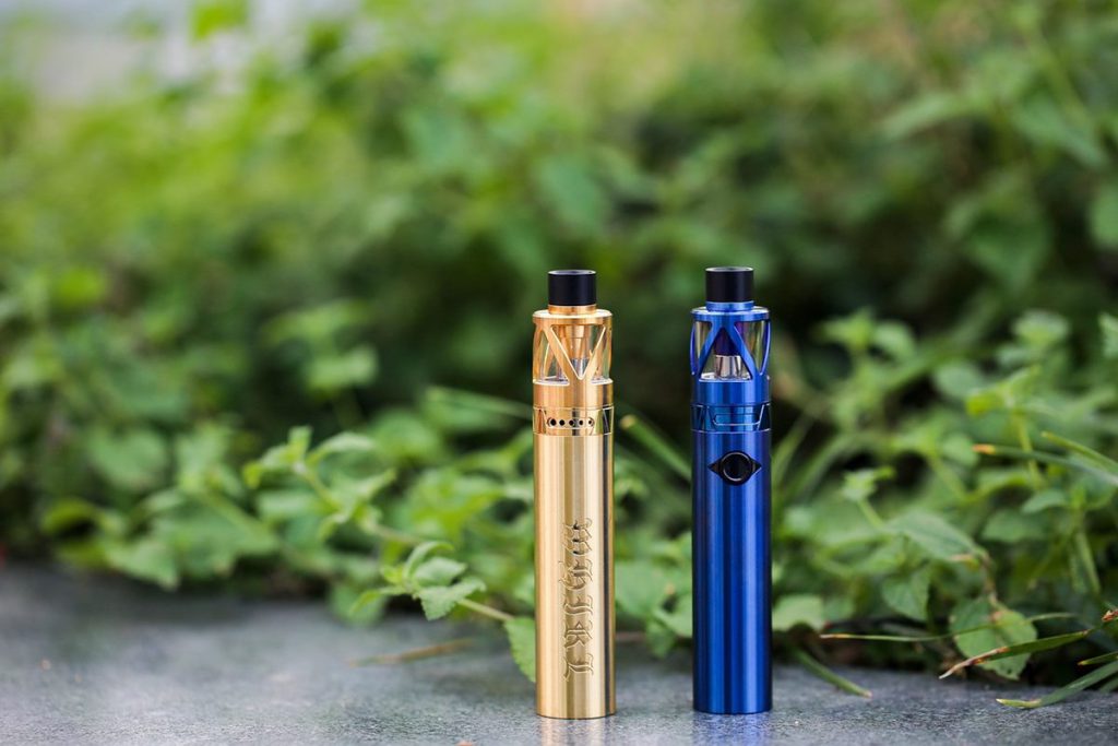 Blue and gold vaporizer pens on concrete path beside bushes