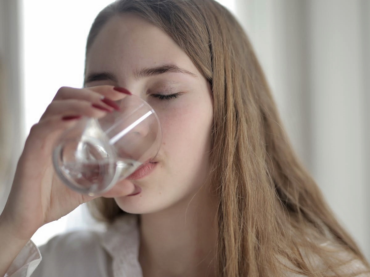 Blonde-haired woman drinking water from clear glass