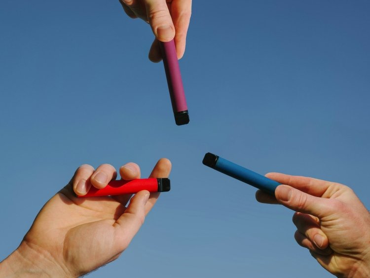 Disposable vaporizers in assorted colors held toward blue sky