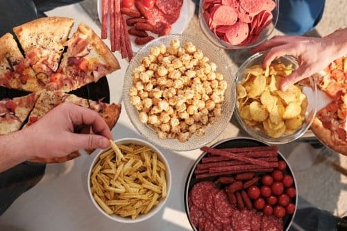 Overhead spread of snacks including pizza, chips and nuts on a table