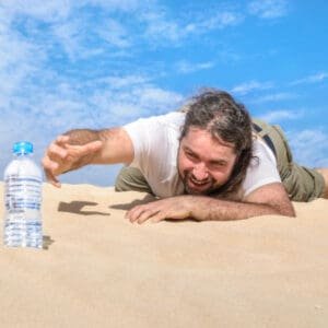 man crawls through desert reaching for water bottle